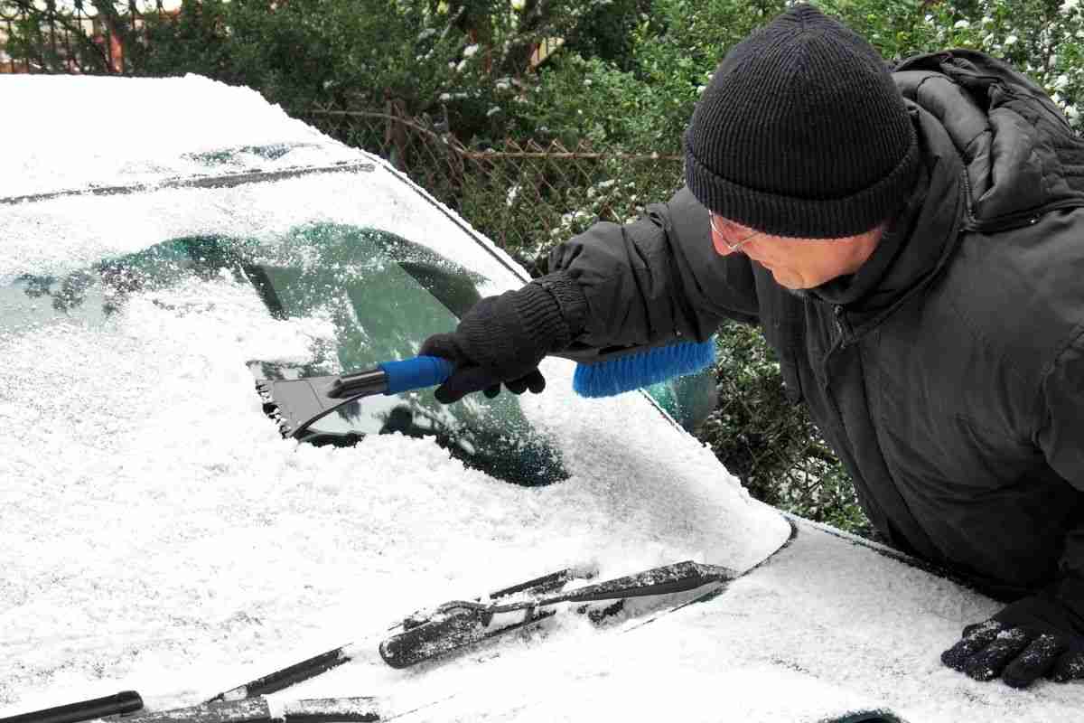 Uomo raschia il ghiaccio dalla propria vettura